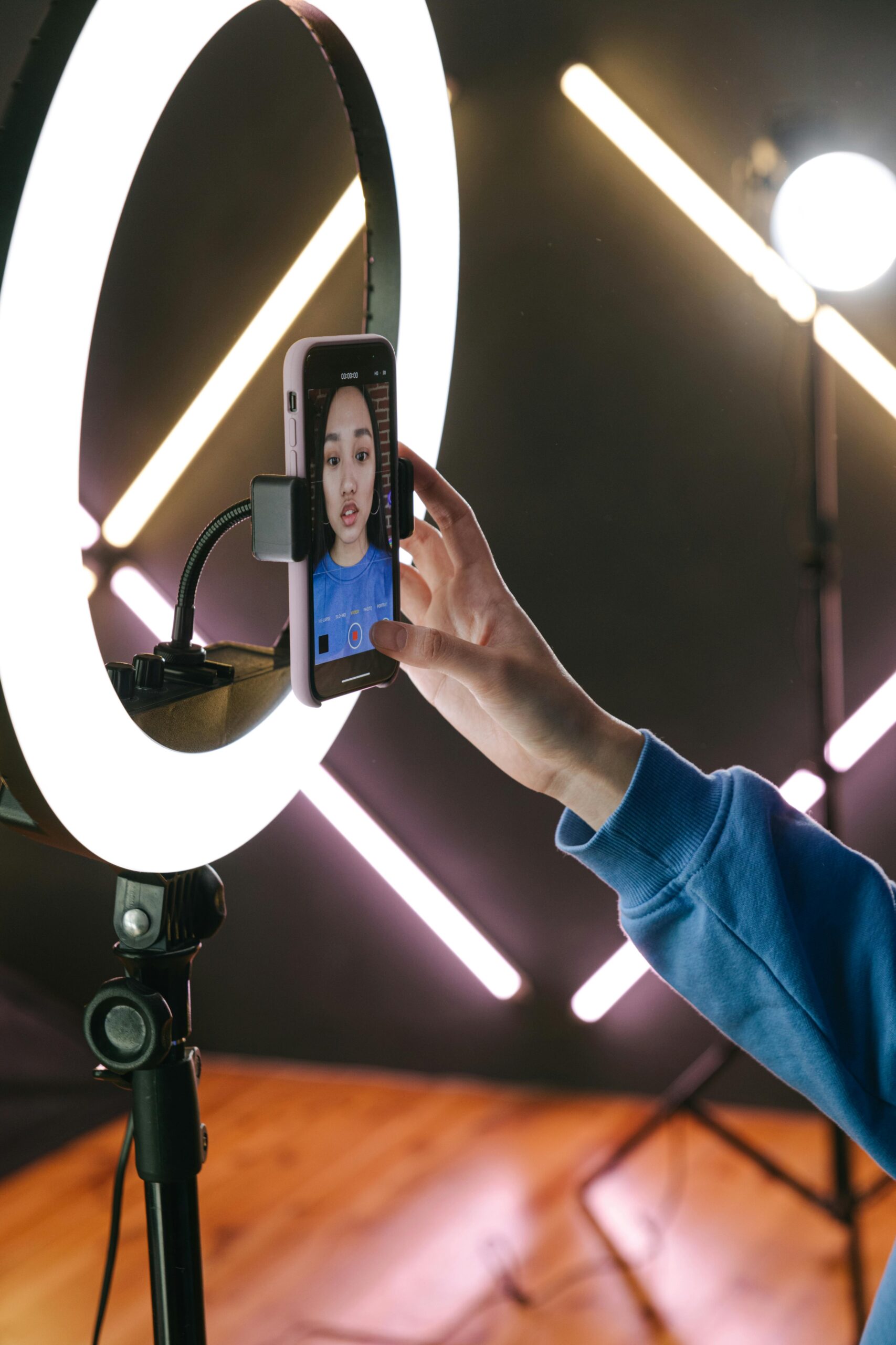 Asian woman using a smartphone and ring light for video streaming indoors, showcasing modern technology.
